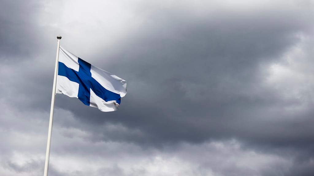 The Finland flag waves proudly against a dramatic, cloudy sky, symbolizing national identity.